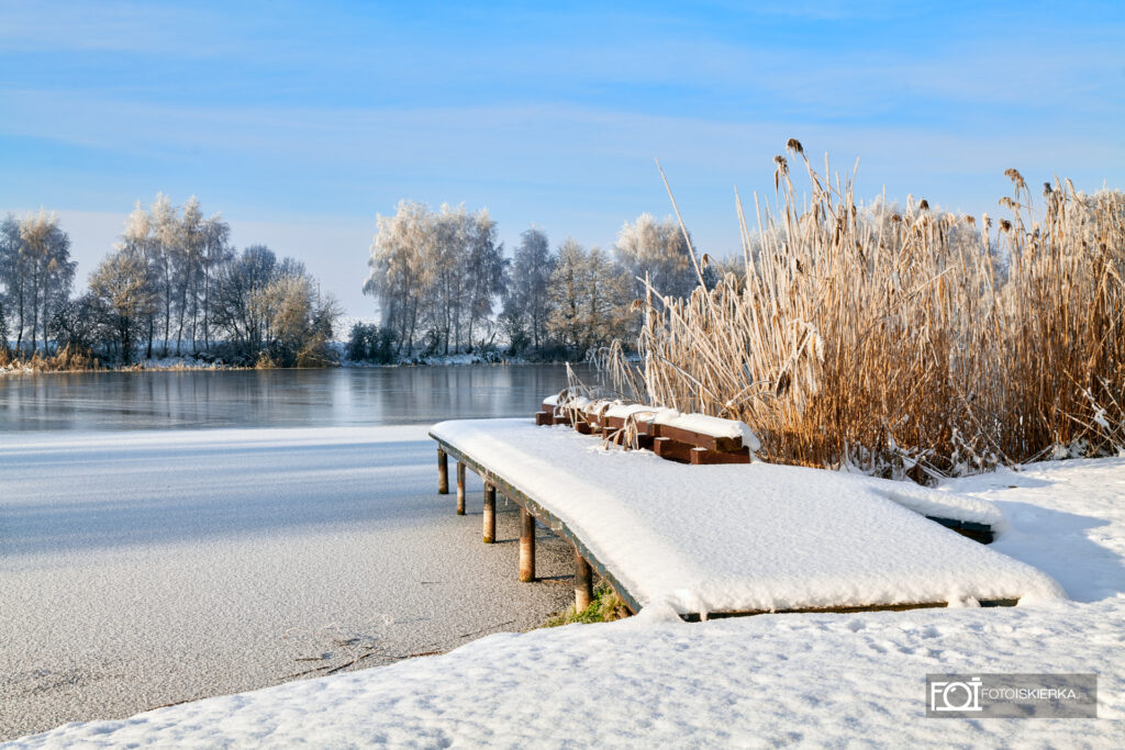 Zima na Mazurach w Polsce w Stanowie. W tle zamarznięte jezioro, ośnieżony pomost