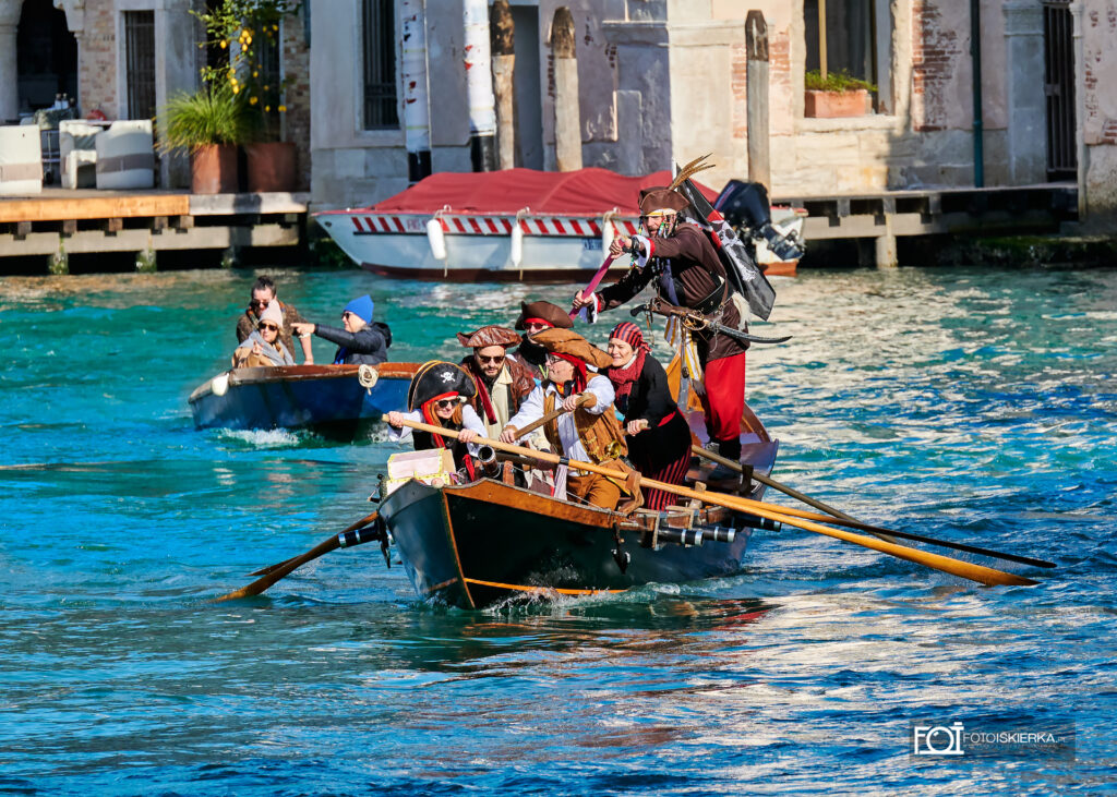 Kolorowa parada łodzi podczas Karnawału w Wenecji. Grupa rekonstruktorów przebranych za piratów płynie tradycyjną drewnianą łodzią po Canal Grande. Na łodzi osobt przebrane za piratów